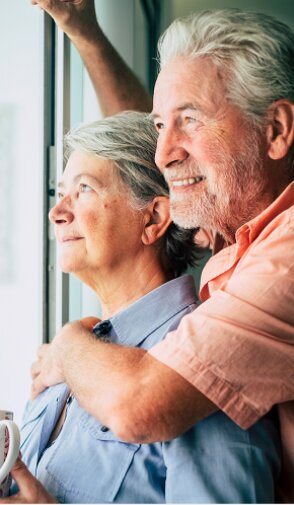 Elderly couple embracing and looking out a window.